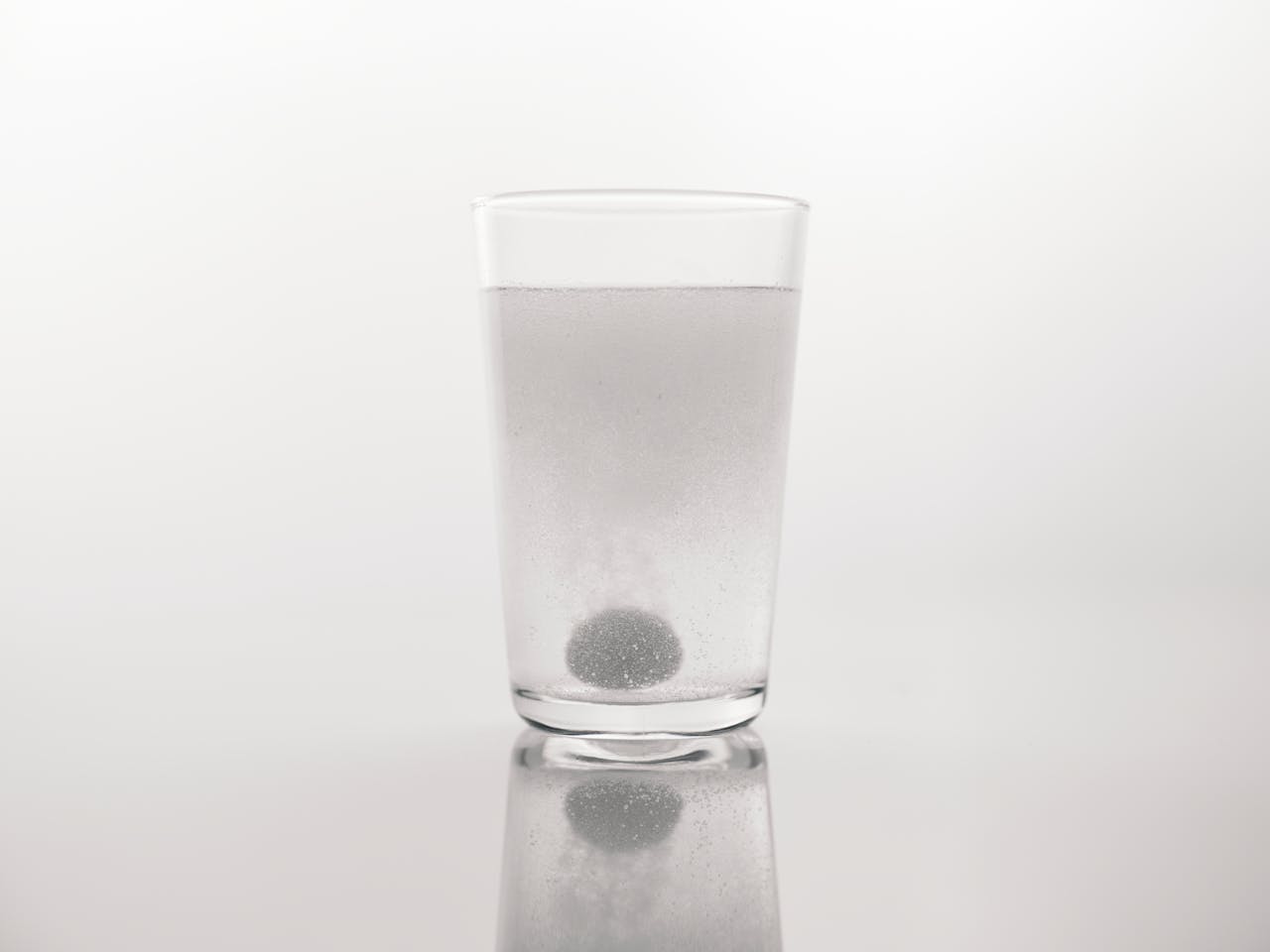 Close-up shot of an effervescent tablet dissolving in a clear glass of water on a white background.