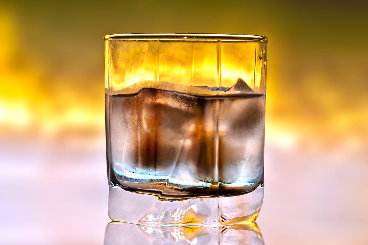services-03 Close-up of a cold refreshing drink in a glass filled with ice cubes, set against a warm background.