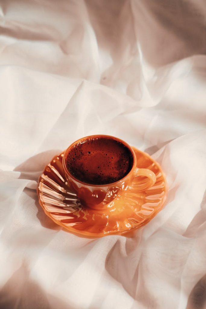 pexels photo 18863033 A vibrant orange coffee cup with saucer sits elegantly on crumpled white satin fabric.
